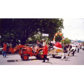 Photograph of library staff driving the tractor, includes library staff walking beside and behind the float