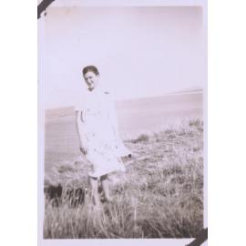 Black and white photo of a woman in a dress with coastal seascape behind